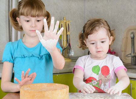 Two sisters sifts the flour to the dough in the kitchenの写真素材