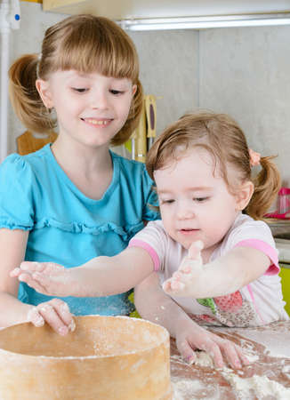 Two sisters sifts the flour to the dough in the kitchenの写真素材