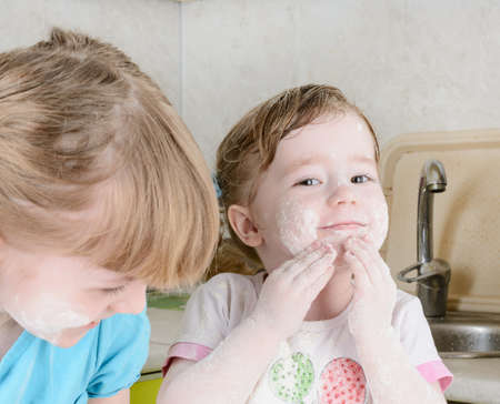 Two sisters sifts the flour to the dough in the kitchenの写真素材