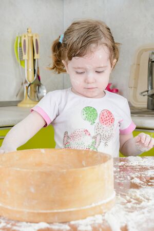 Little girl sifts the flour for the doughの写真素材