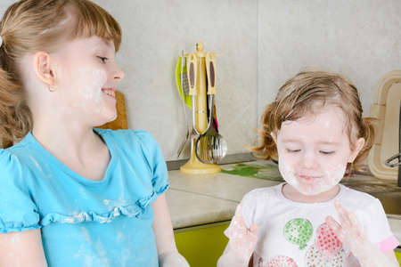 Two sisters sifts the flour to the dough in the kitchenの写真素材