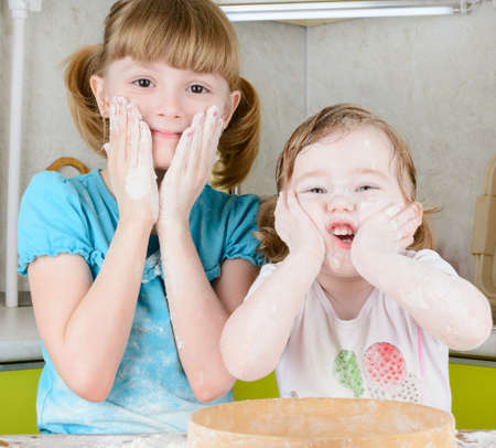 Two sisters sifts the flour to the dough in the kitchenの写真素材
