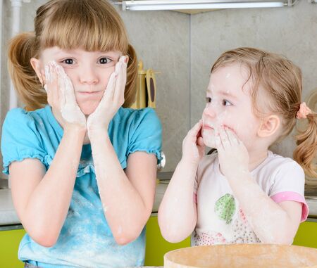 Two sisters sifts the flour to the dough in the kitchenの写真素材