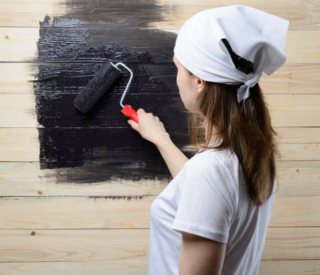 Woman painter paint roller wooden wall in blackの写真素材