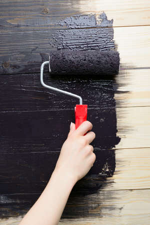Female hand with roller paint wooden wall in blackの写真素材