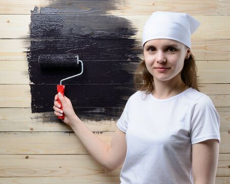 Woman painter paint roller wooden wall in blackの写真素材