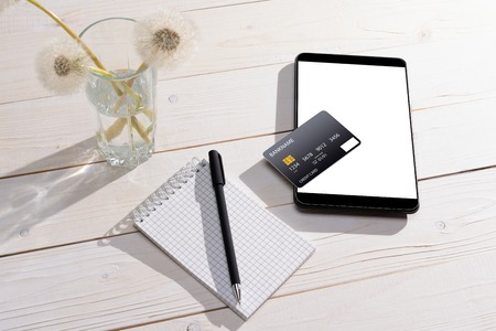 Credit card, tablet and notebook with a pen on a white wooden tableの写真素材