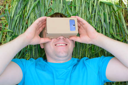 Young man lying in a field and looks into a virtual reality glassesの写真素材