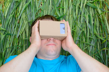 Young man lying in a field and looks into a virtual reality glassesの写真素材