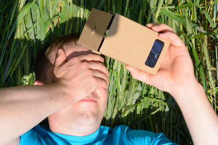 Young man lying in a field and looks into a virtual reality glassesの写真素材