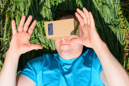 Young man lying in a field and looks into a virtual reality glassesの写真素材