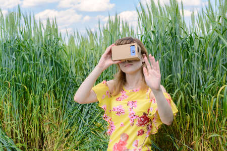 Young woman sitting on the grass in the field and looks into a virtual reality glassesの写真素材