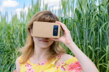 Young woman sitting on the grass in the field and looks into a virtual reality glasses