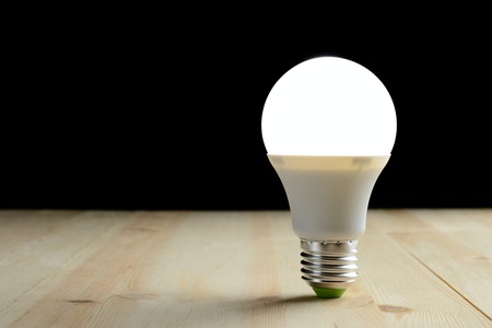 LED lamp standing on a wooden table on a black backgroundの写真素材