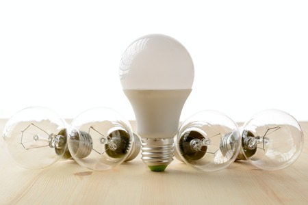 LED lamp standing on a wooden table, near an incandescent lamp lie