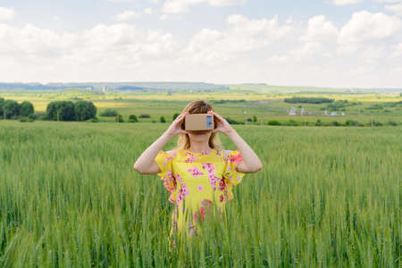 Young woman standing in a field and looks into a virtual reality glasses