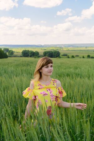 Young woman standing in a field among green rye on a summer dayの写真素材