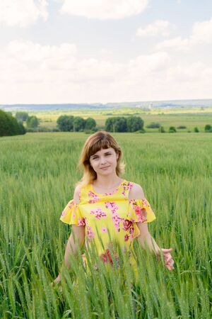 Young woman standing in a field among green rye on a summer dayの写真素材