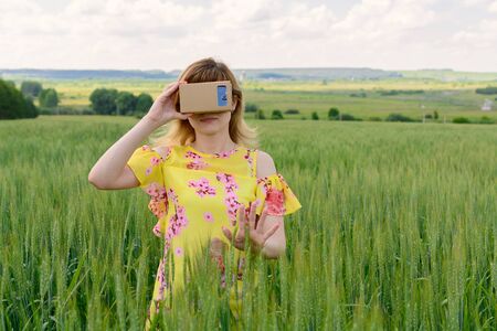 Young woman standing in a field and looks into a virtual reality glassesの写真素材
