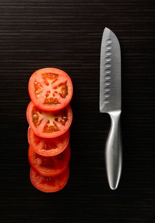 Cut tomato and cucumber with a knife lie on a dark tileの写真素材