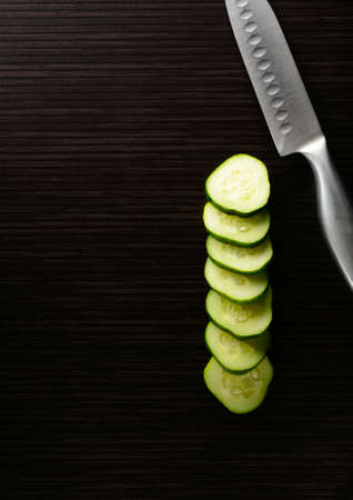 Cut cucumber with a knife lie on a dark tileの写真素材