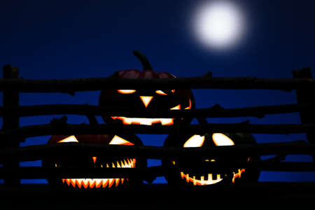 Three Halloween pumpkin with scary face behind the old wooden fenceの写真素材