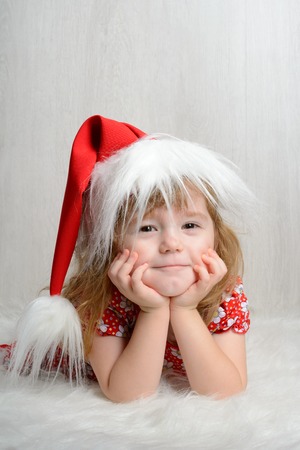 Portrait of a little girl in a santa hat on a white background wooden wallの写真素材