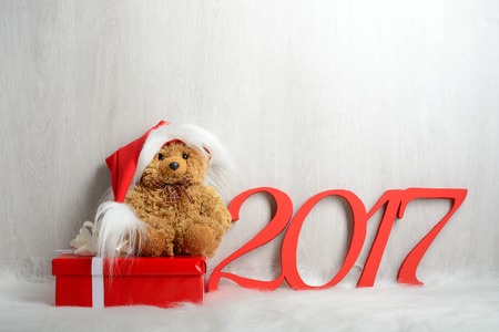 Teddy bear in santa hat with presents sitting on a white carpetの写真素材