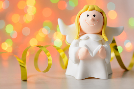 Toy angel with book in hand on the background of blurred lights garlandの写真素材