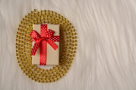 Gift box with red bow and gold beads on a fur rugの写真素材