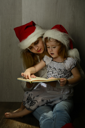 Little girl in the lap of mother in santa hat reading a bookの写真素材