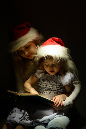 Little girl in the lap of mother in santa hat reading a bookの写真素材
