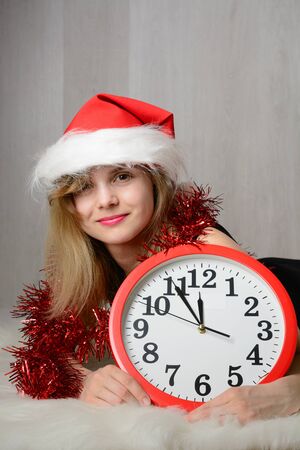 Girl in santa hat lying on a fur rug next to the clockの写真素材