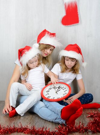 Young woman with her two daughters in a santa hat looking at his watchの写真素材