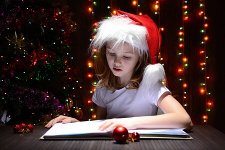 Girl in santa hat reading a book on a background of luminous garlandsの写真素材