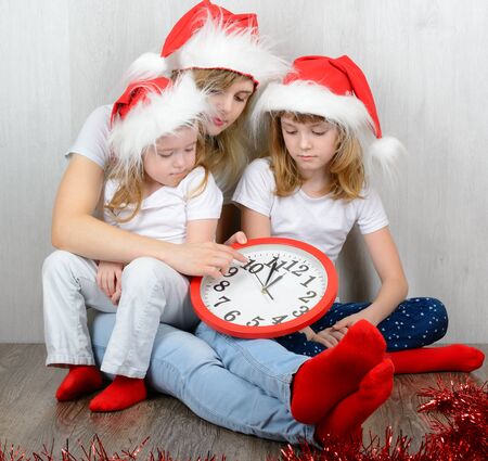Young woman with her two daughters in a santa hat looking at his watchの写真素材