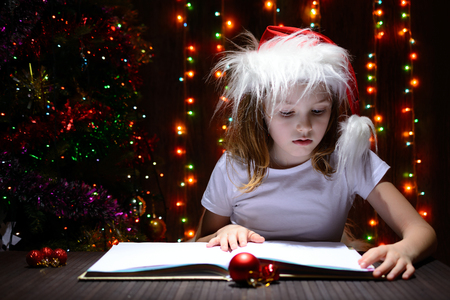 Girl in santa hat reading a book on a background of luminous garlandsの写真素材