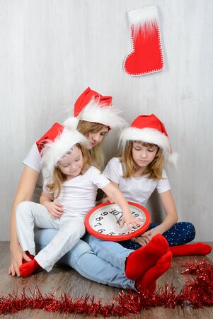 Young woman with her two daughters in a santa hat looking at his watchの写真素材