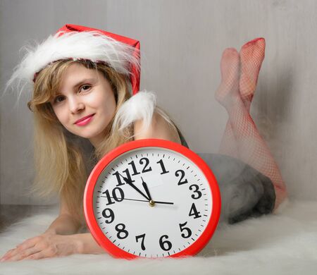Girl in santa hat lying on a fur rug next to the clockの写真素材