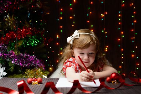 Little girl with red pencil writes a letter to Santa Clausの写真素材