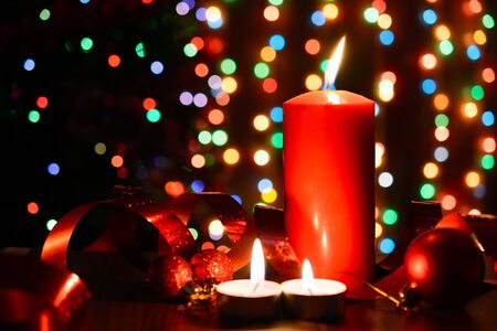 Burning candle on a table with Christmas decorations on a background garlandsの写真素材