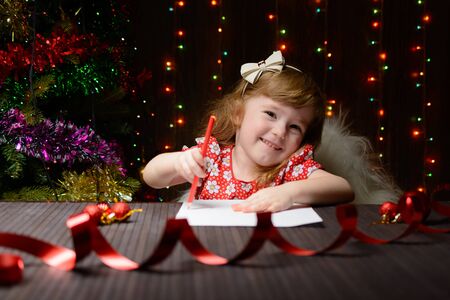 Little girl with red pencil writes a letter to Santa Clausの写真素材