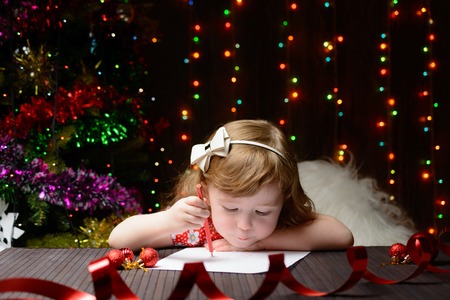 Little girl with red pencil writes a letter to Santa Clausの写真素材