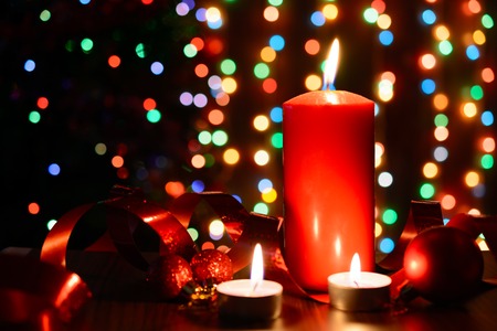 Burning candle on a table with Christmas decorations on a background garlandsの写真素材