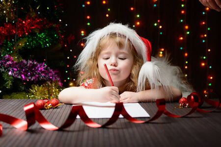 Little girl with red pencil writes a letter to Santa Clausの写真素材