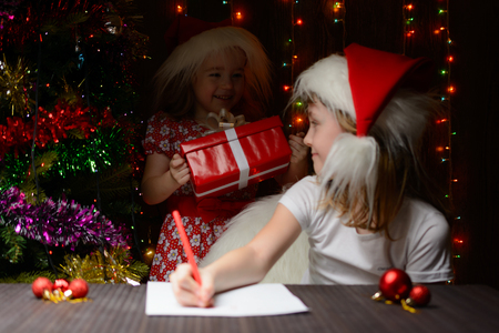 Girl in santa hat writing a letter, in the back is the younger sister with a giftの写真素材