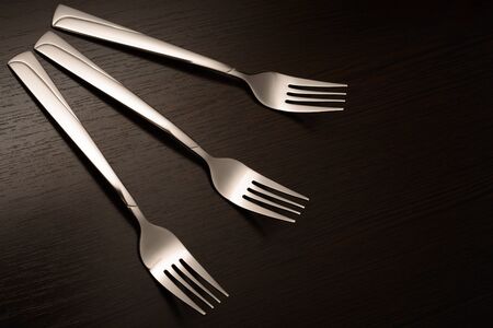 Three metal forks on a dark wooden table