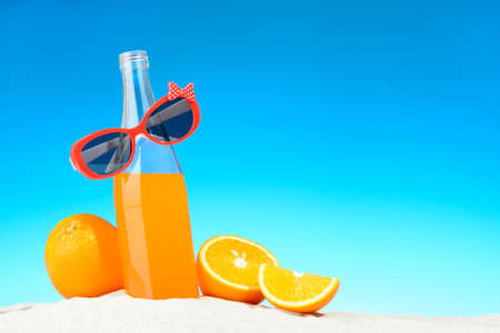 The bottle of orange juice and sunglasses on the beachの写真素材