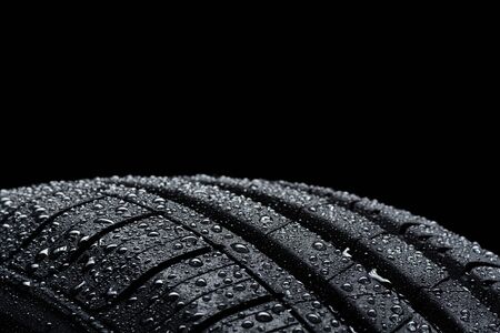 Car tire covered with water drops on black background