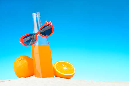 The bottle of orange juice and sunglasses on the beachの写真素材